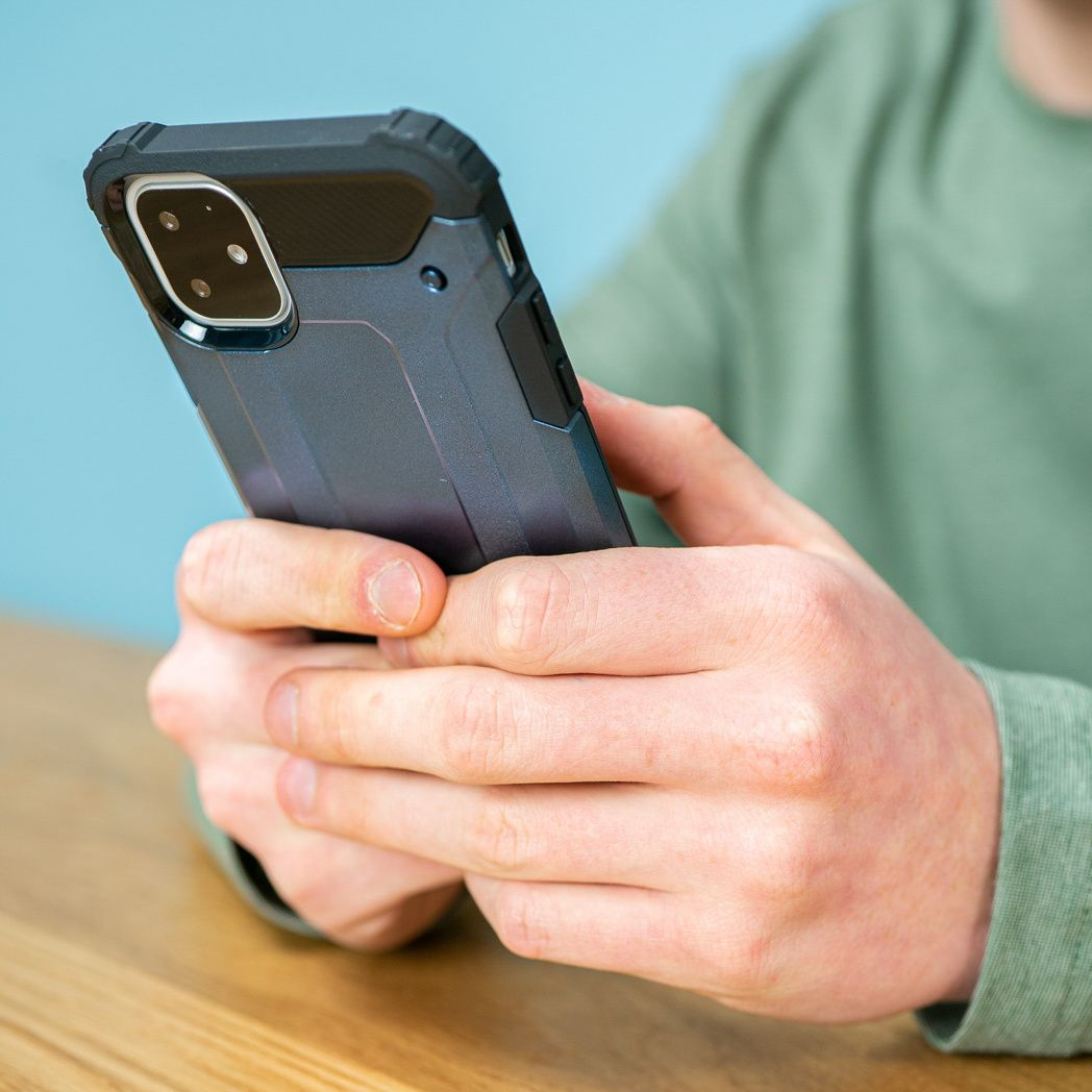 Une personne tient un smartphone dans un étui de protection. Le téléphone est noir et la personne porte une chemise verte.