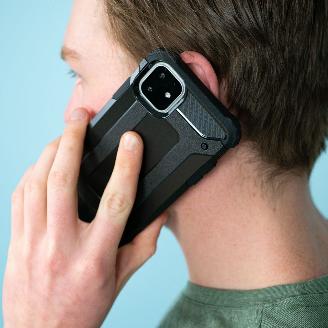 Een man houdt een zwarte telefoon tegen zijn oor. De telefoon heeft een beschermhoesje. De achtergrond is lichtblauw.