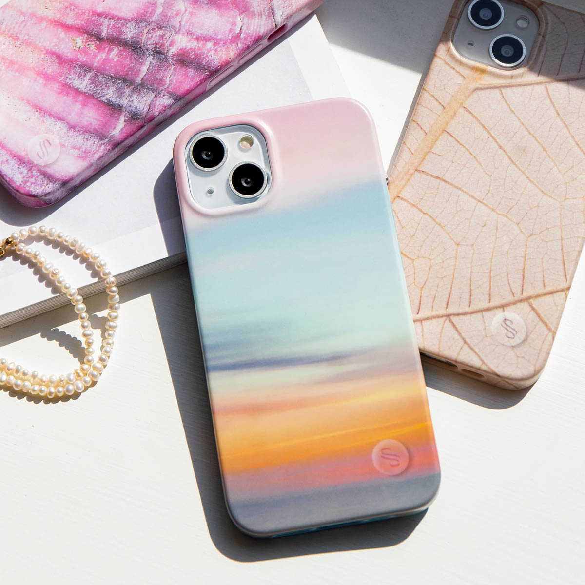 Verschillende telefoonhoesjes met verschillende ontwerpen en kleuren zijn gerangschikt op een wit oppervlak met een parelketting.