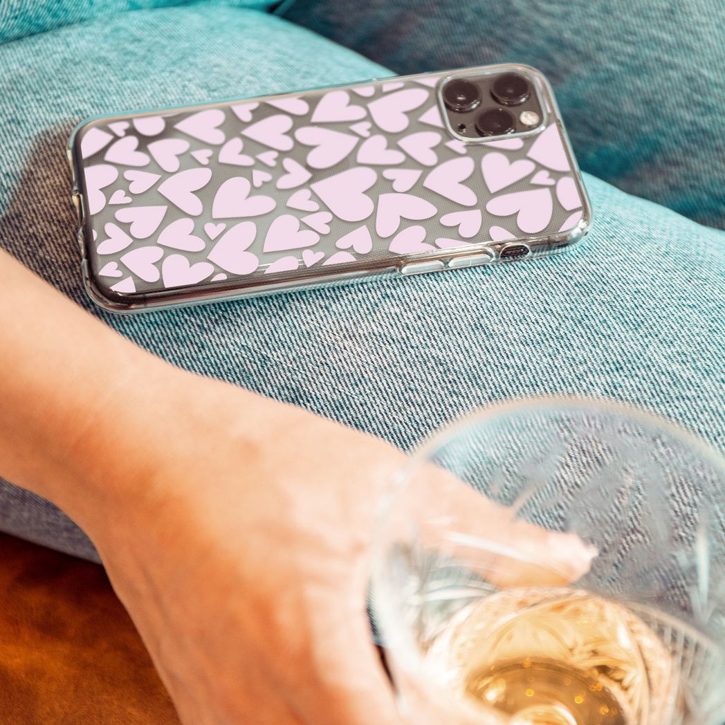 Un téléphone avec des cœurs roses sur les genoux, une main tenant un verre de liquide, le tout sur un jean. L'arrière-plan est flou.