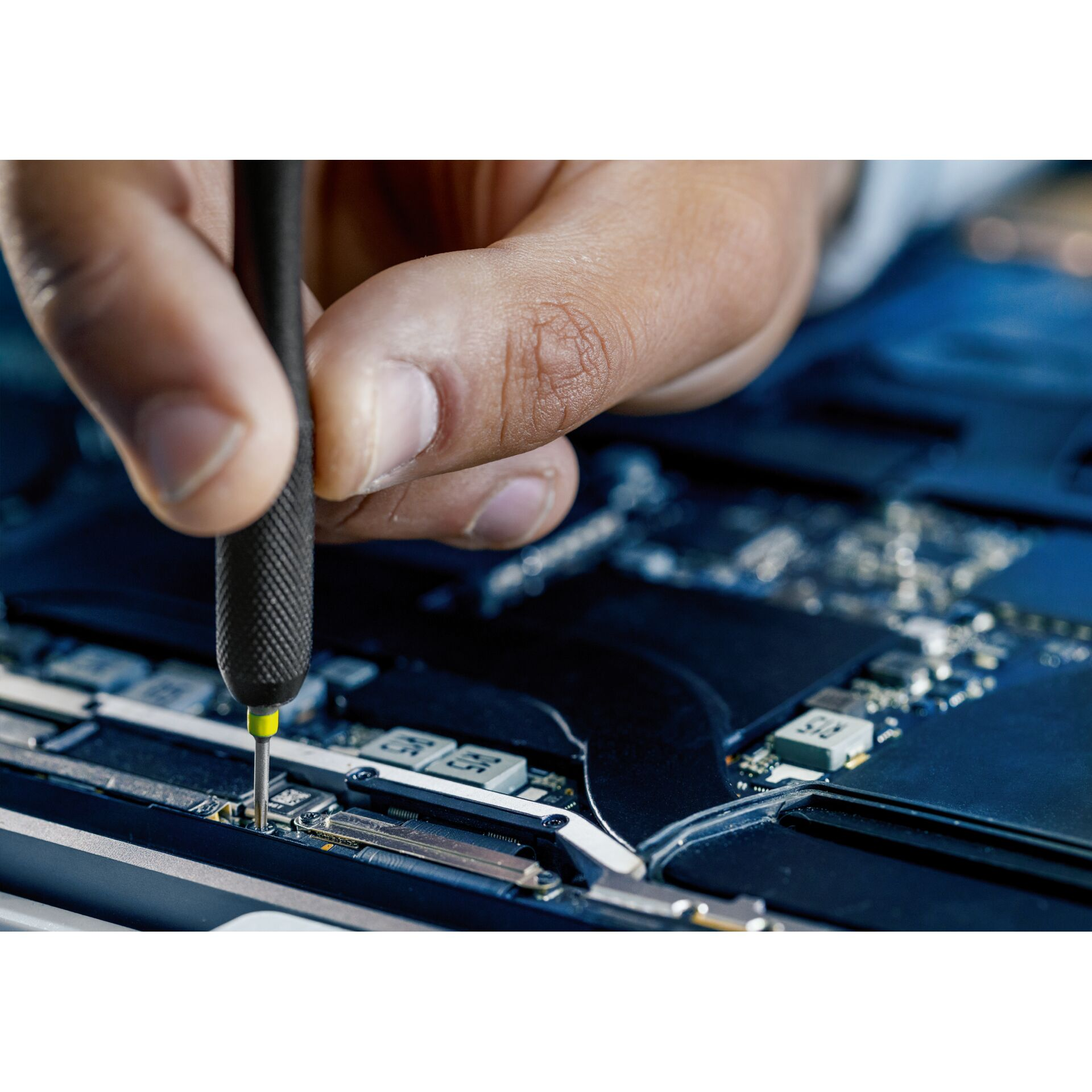 Eine Hand benutzt einen Schraubenzieher auf einer Platine. Der Schraubenzieher zeigt nach unten. Die Szene ist nah dran.