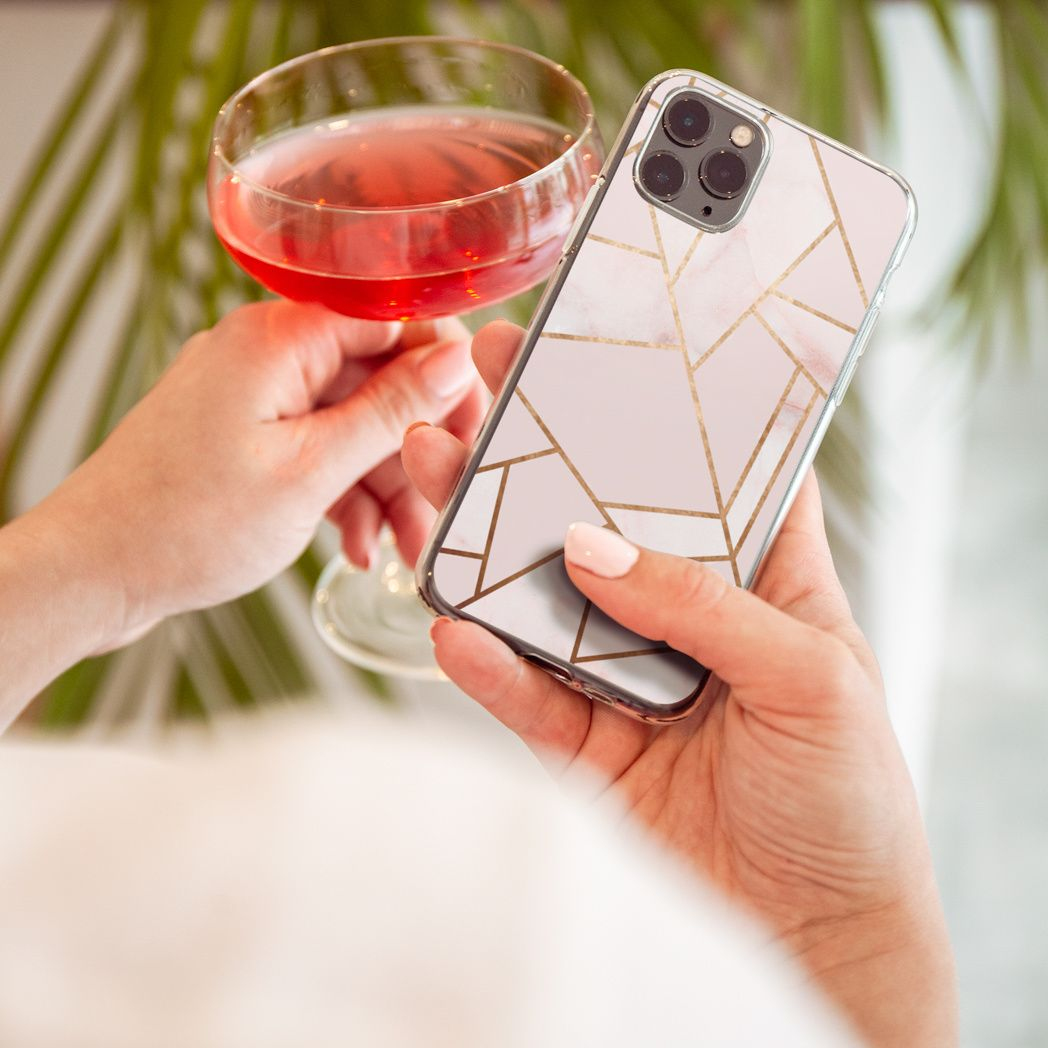 Persoon houdt een telefoon met een geometrisch ontwerp en een glas roze vloeistof vast. Achtergrond heeft een groene plant.