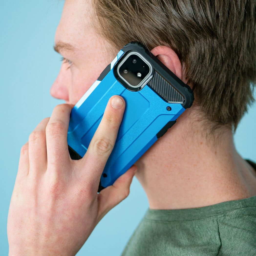Een man houdt een blauwe telefoon tegen zijn oor. De telefoon zit in een beschermhoes. Hij draagt een groen shirt tegen een blauwe achtergrond.