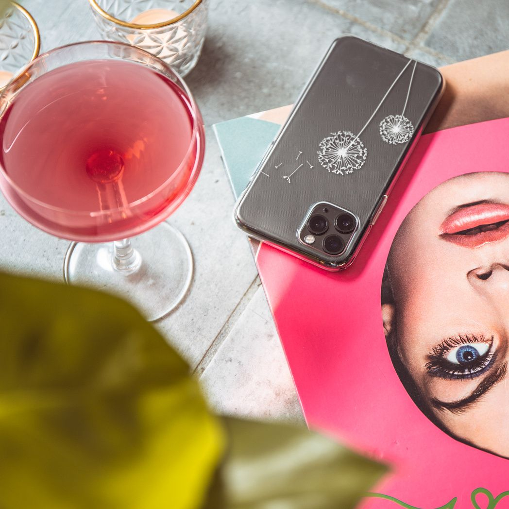 Un cocktail in un bicchiere, un telefono con un design a dente di leone e una rivista con il volto di una donna, il tutto su una superficie piastrellata.