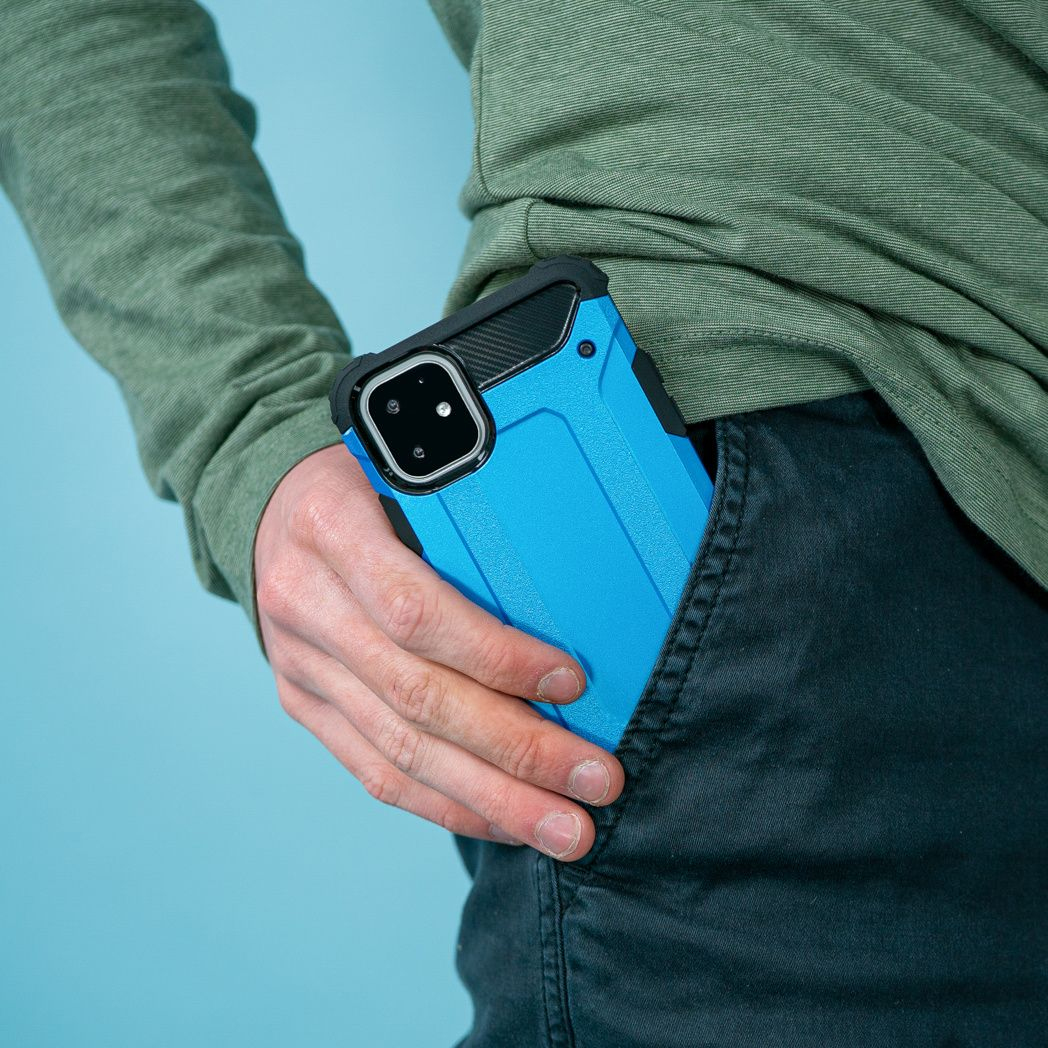Een persoon stopt een blauwe telefoonhoes in zijn zak. De persoon draagt een groen shirt en een zwarte broek.