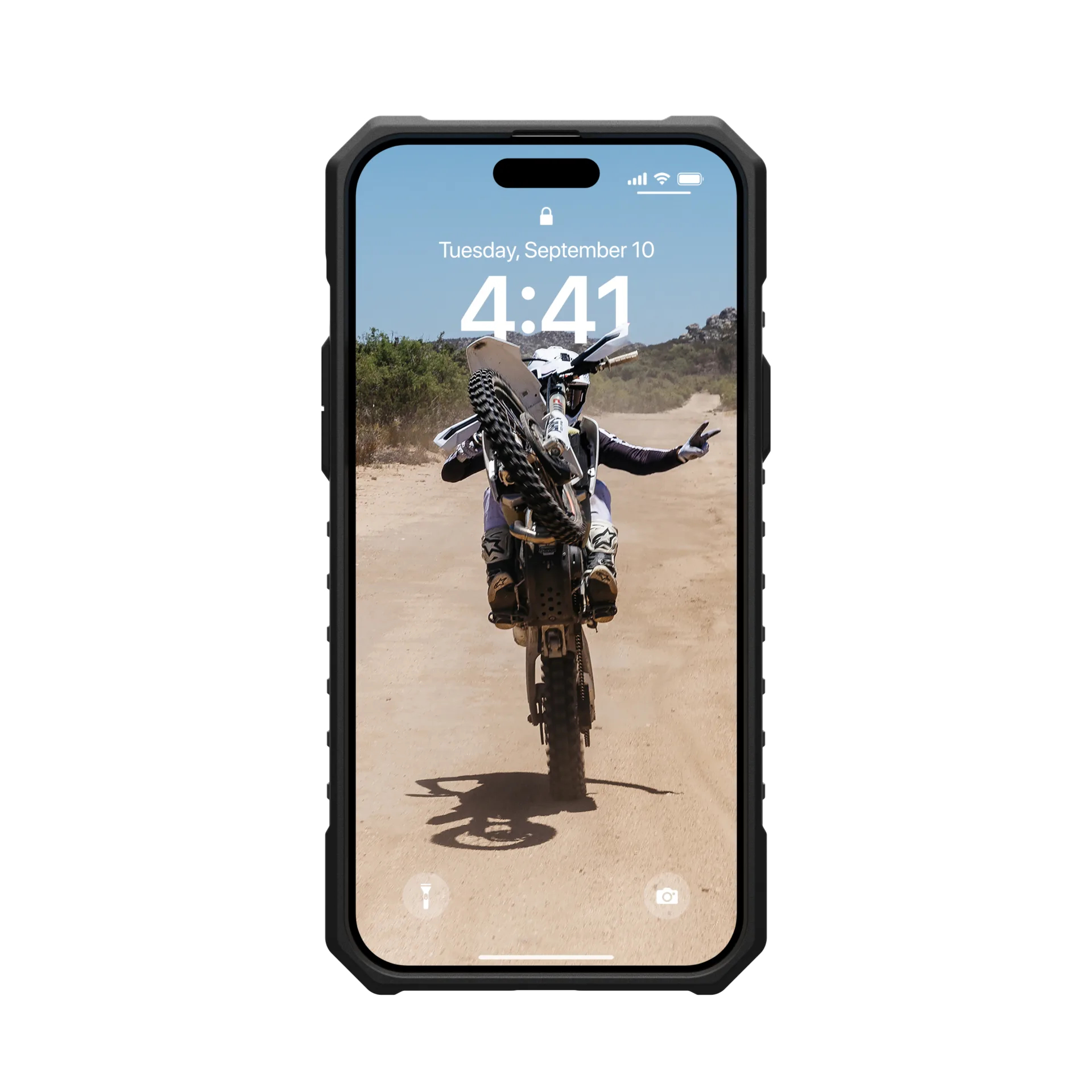 Ein Telefon zeigt eine Person auf einem Motorrad, die einen Wheelie auf einer unbefestigten Straße macht, mit blauem Himmel im Hintergrund.