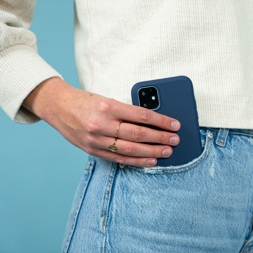 Une personne portant un pull blanc et un jean, tenant un téléphone bleu marine dans sa poche. Une bague en or est visible.