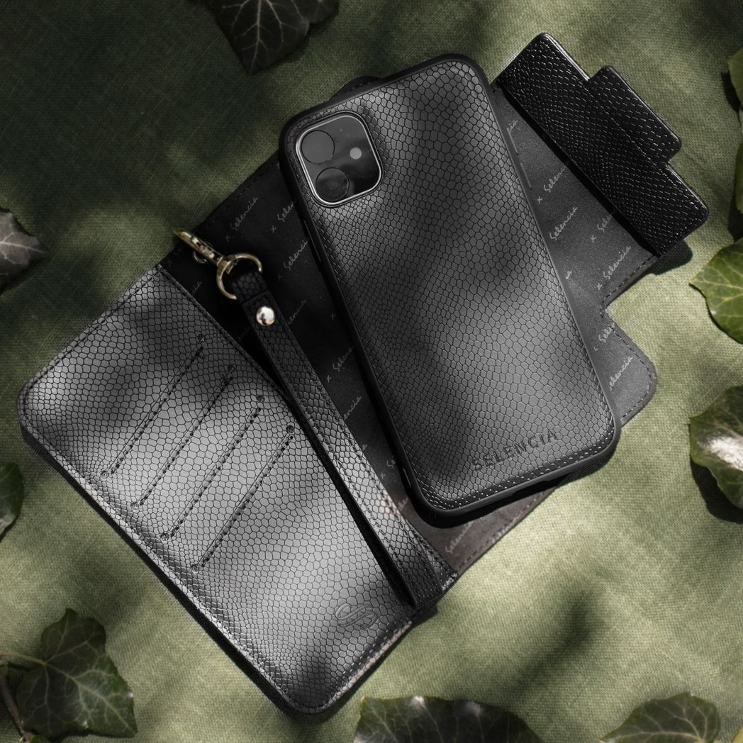 Coque de téléphone, portefeuille et bracelet noirs sur une surface verte avec des feuilles. Tous ont un motif texturé. Le téléphone est dans l'étui.