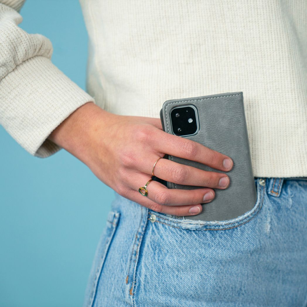 Una persona con maglione e jeans tiene in tasca una custodia grigia per telefono. Un anello d'oro al dito. Sfondo blu.