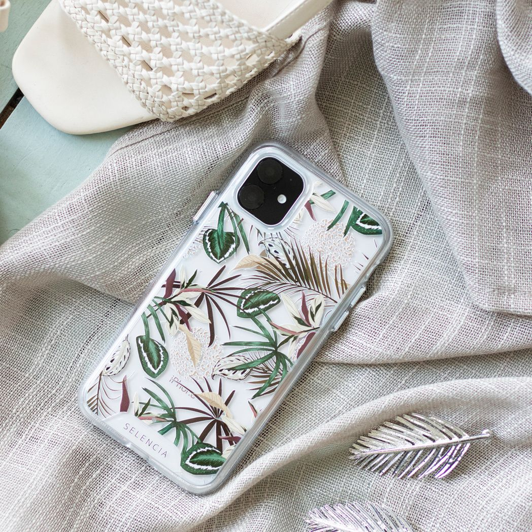 Une coque de téléphone avec un motif floral est posée sur du tissu, près de sandales. Une décoration de feuille argentée est également présente.