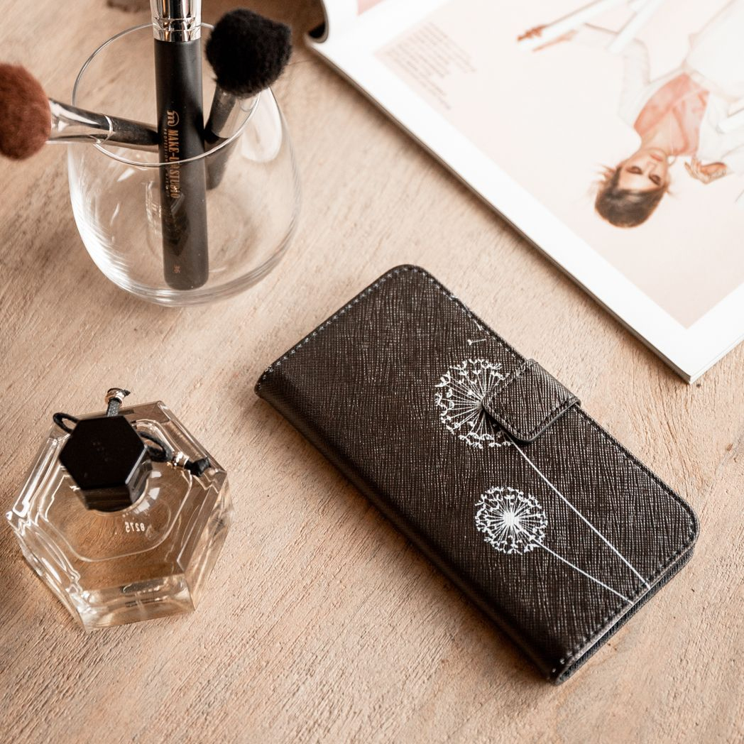 Make-up borstels in een glas, een parfumflesje en een telefoonhoesje met paardenbloemmotieven op een houten oppervlak.