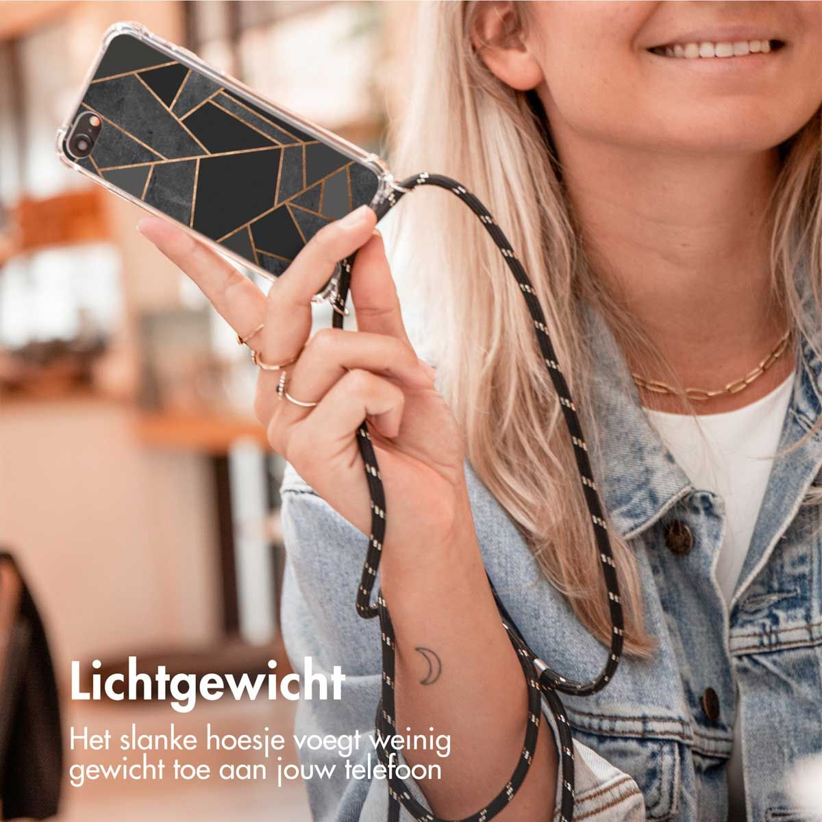 Een vrouw houdt een telefoon vast in een hoesje met een zwart en goud geometrisch ontwerp. De telefoon heeft een koord. Ze draagt een spijkerjasje en lacht.