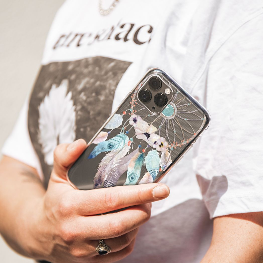 Una persona tiene in mano un telefono con un design acchiappasogni. Il telefono ha una custodia trasparente con piume. La persona indossa una camicia bianca.