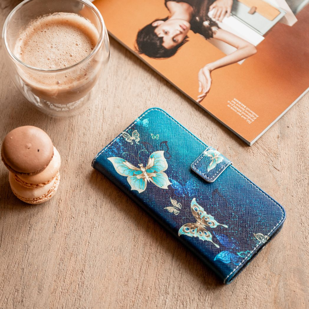 Une coque de téléphone avec motif papillon, macarons, café dans un verre et un magazine sur surface en bois.