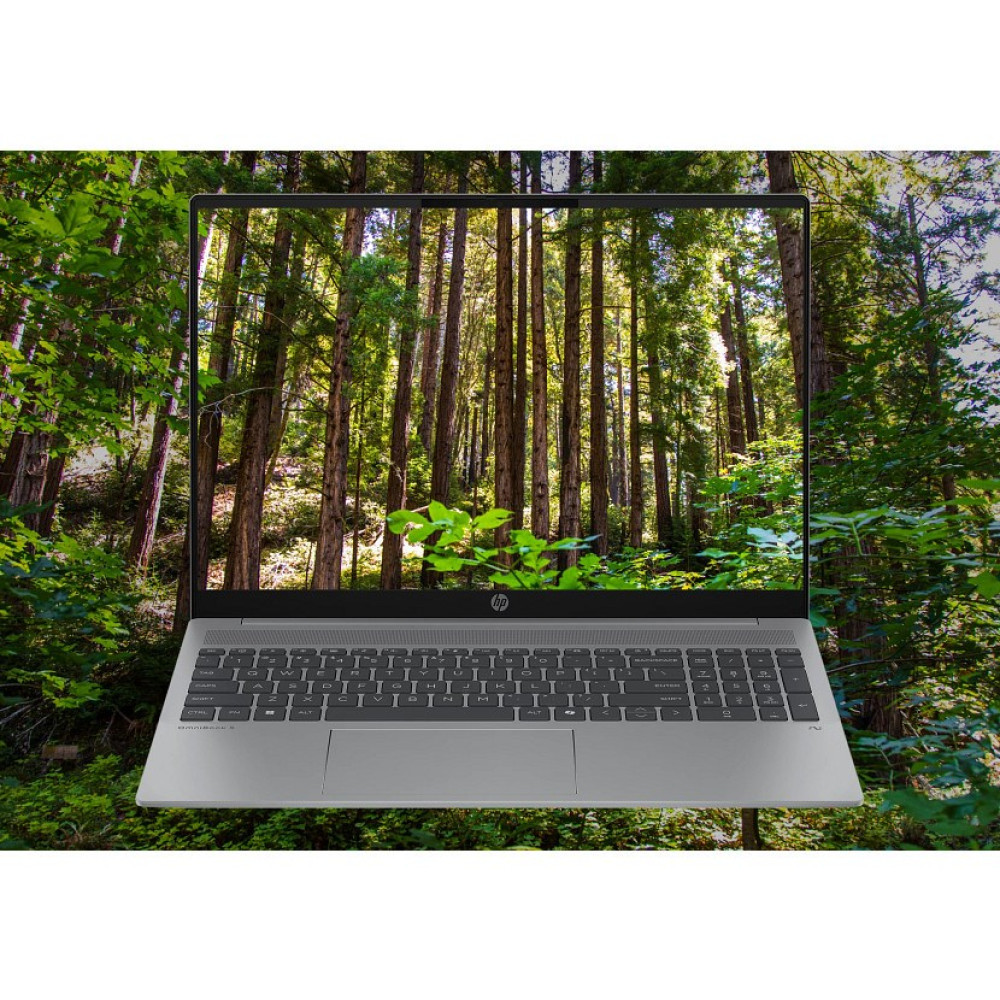 Laptop wyświetla scenę leśną. Klawiatura laptopa jest widoczna, na tle zielonych liści i lasu.