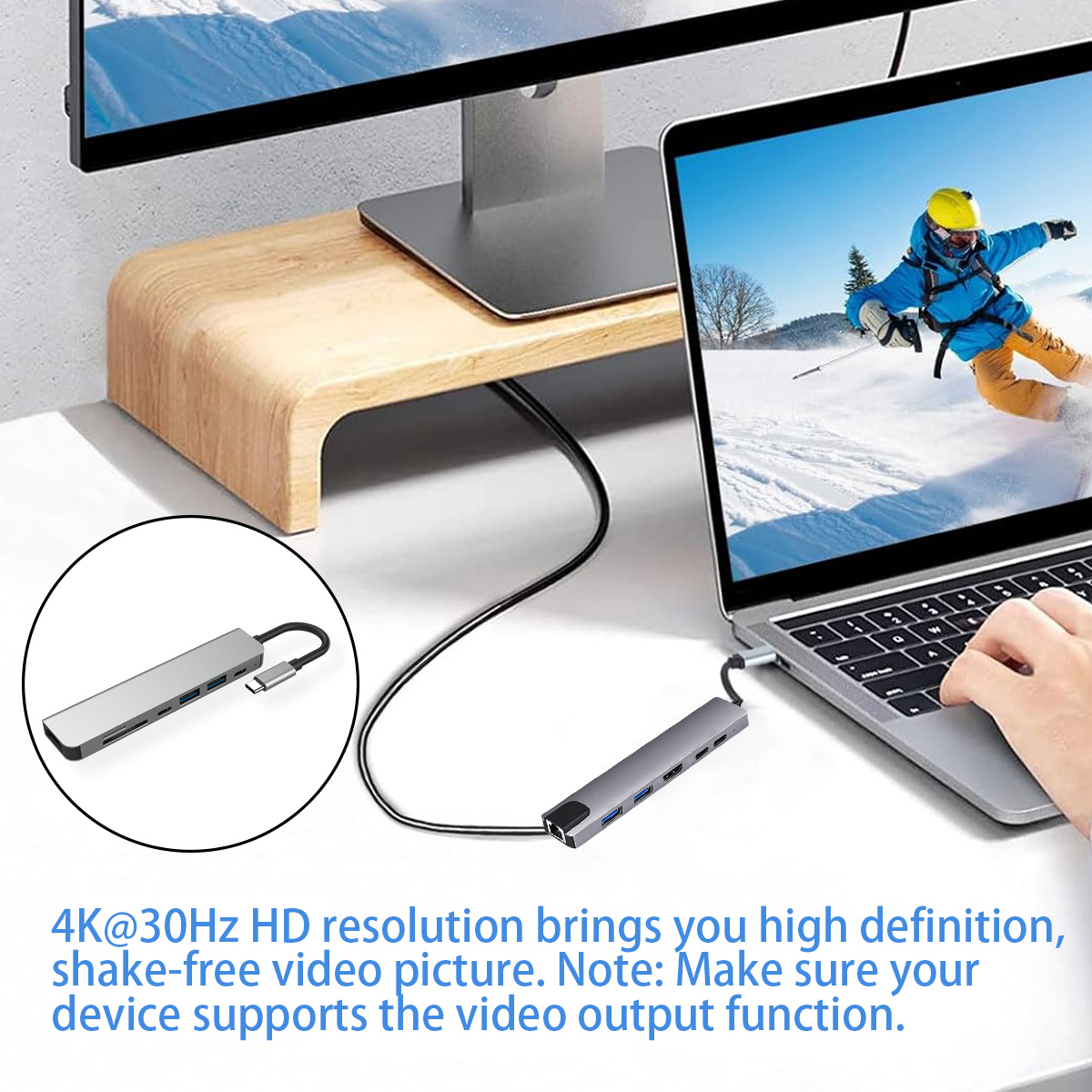 Ein Laptop ist mit einem grauen Hub verbunden. Auf dem Bildschirm ist ein Skifahrer zu sehen. Ein Monitor und ein Holzständer sind im Hintergrund.