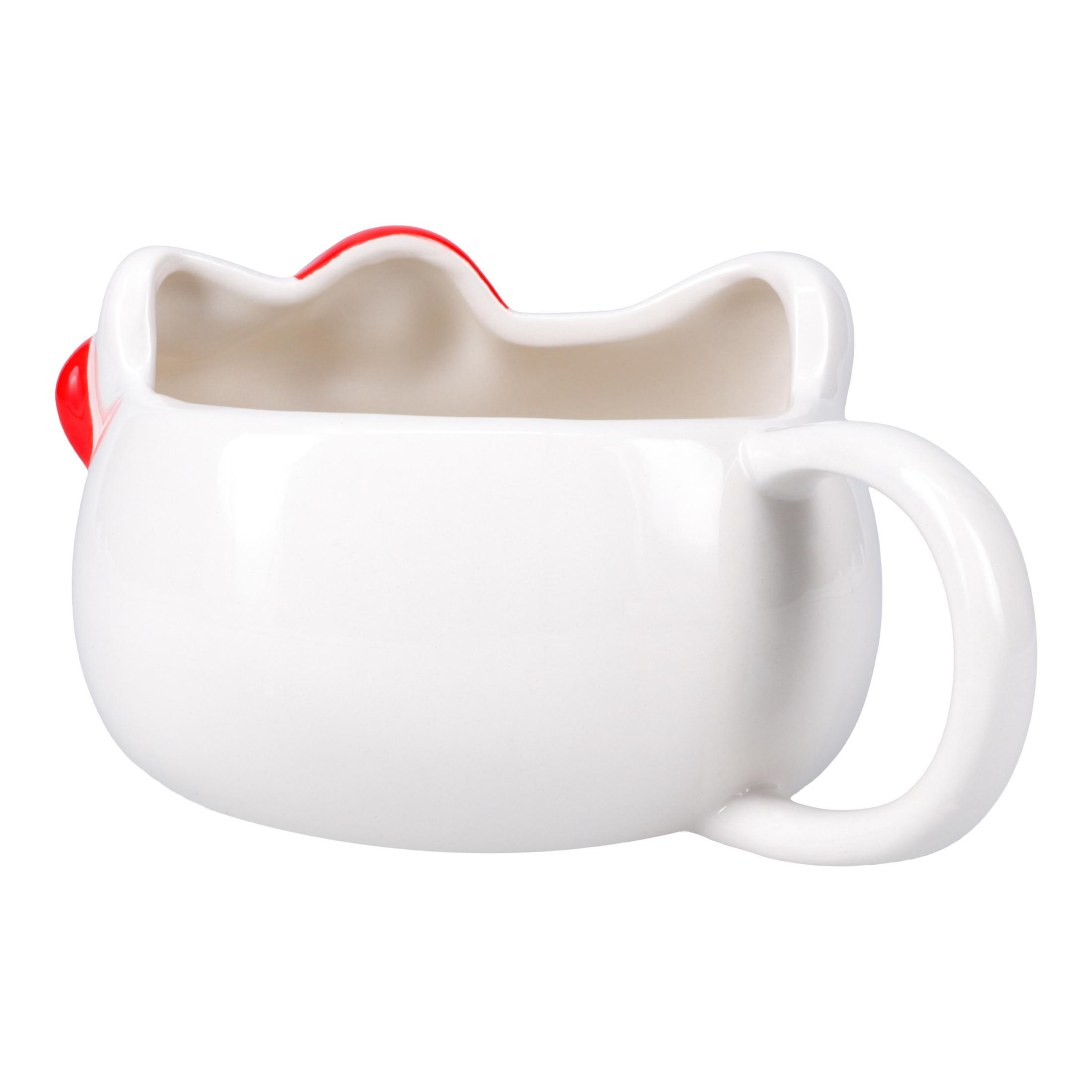 Biały ceramiczny kubek w kształcie głowy Hello Kitty. Ma czerwoną kokardę i uchwyt. Tło jest białe.
