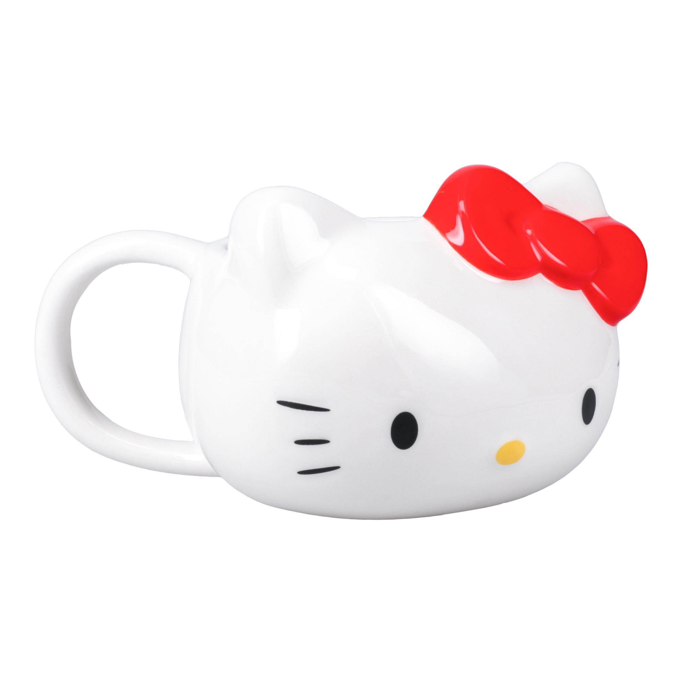 Biały kubek Hello Kitty z czerwoną kokardą. Ma czarne oczy i wąsy. Kubek stoi na białym tle.