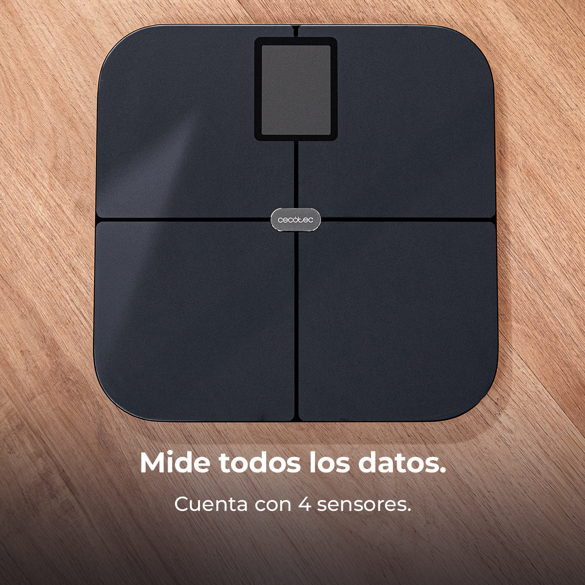 Una báscula digital negra con pantalla está sobre una superficie de madera. La báscula tiene cuatro sensores y la marca es visible.