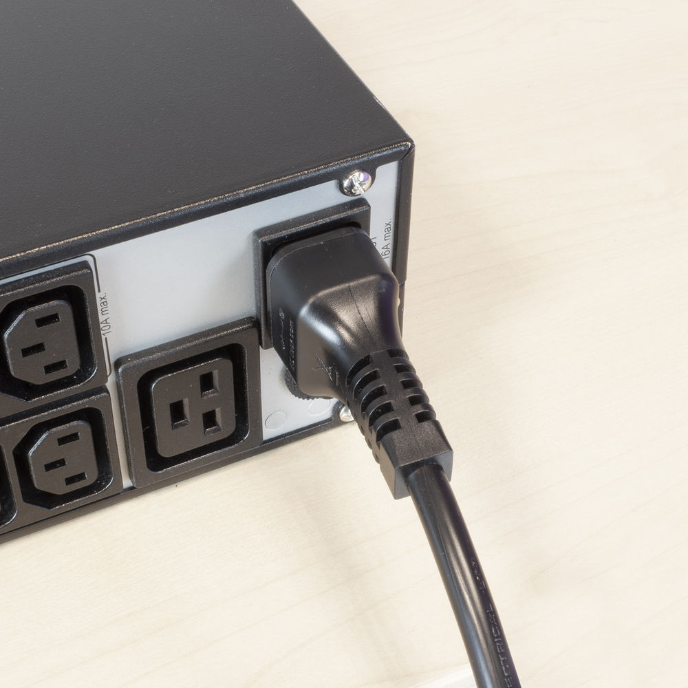 Ein schwarzes Netzkabel ist in eine schwarze Steckdosenleiste eingesteckt. Mehrere Steckdosen sind sichtbar. Der Hintergrund ist eine helle Holzoberfläche.