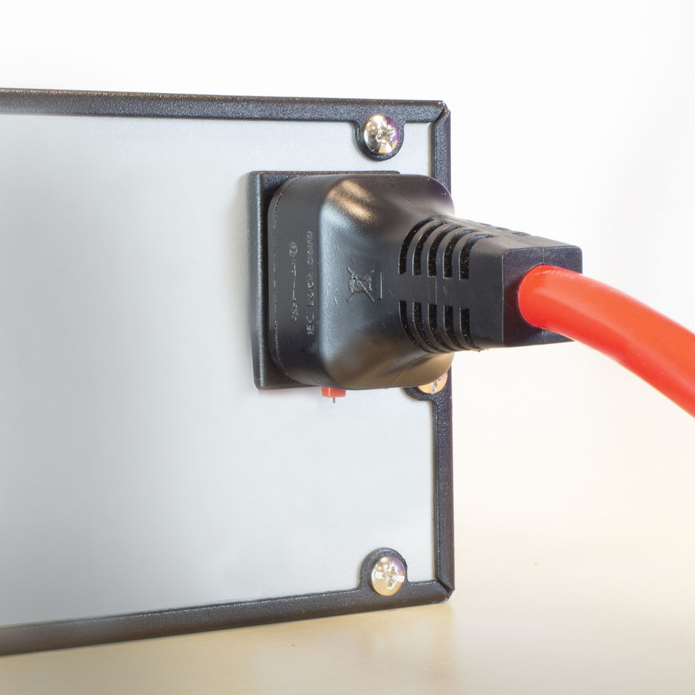 Schwarzer Netzstecker in eine graue Platte mit rotem Kabel gesteckt. Platte liegt auf Holz.
