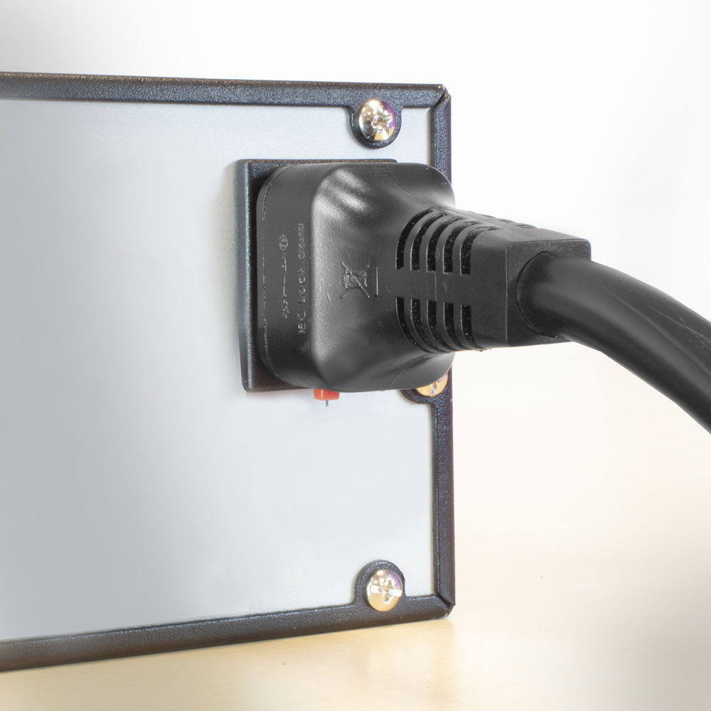 Ein schwarzer Netzstecker steckt in einem silbernen rechteckigen Gerät. Das Gerät hat einen schwarzen Rand und befindet sich auf hellem Hintergrund.