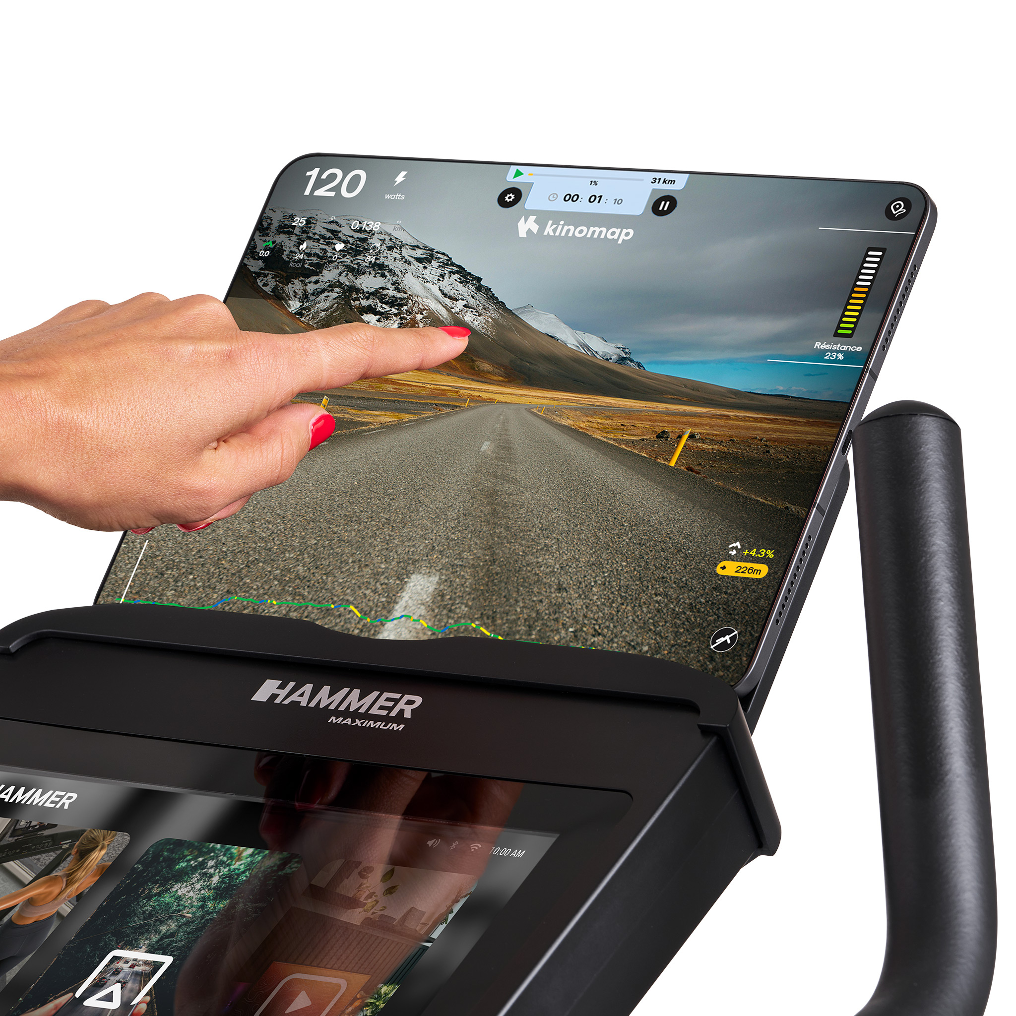 Eine Hand berührt einen Tablet-Bildschirm mit einer Straßenszene. Das Tablet befindet sich auf einem schwarzen Trainingsrad. Roter Nagellack.
