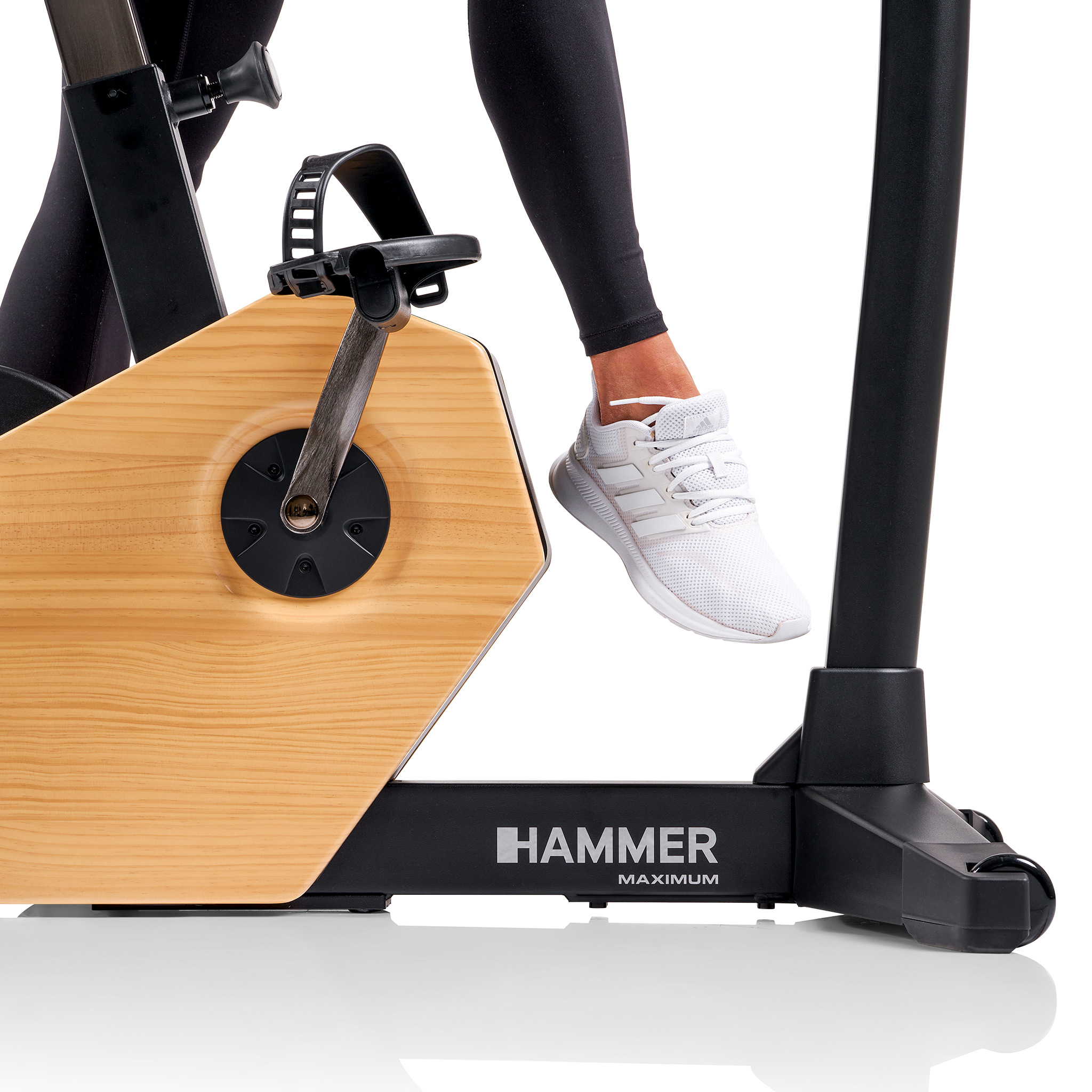Bein einer Person auf einem Heimtrainer. Das Fahrrad ist helles Holz und schwarz. Weißer Schuh auf dem Pedal.