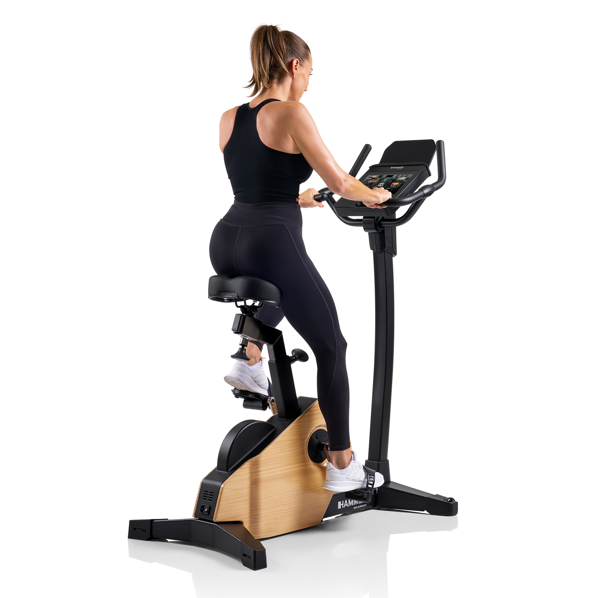 Frau auf Heimtrainer. Sie trägt schwarze Sportkleidung. Das Fahrrad ist schwarz mit Holzverkleidung.
