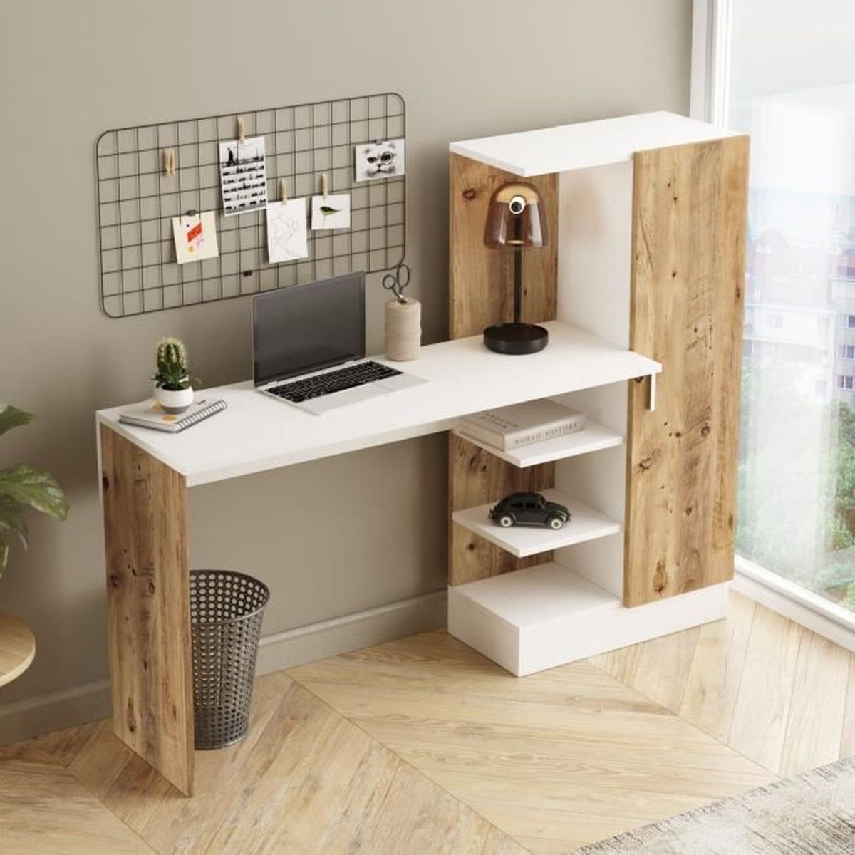 Ein moderner Schreibtisch mit Laptop, Lampe und Dekorationsartikeln. Ein Mülleimer und ein Holzschrank sind ebenfalls zu sehen. Im Hintergrund ist ein Fenster.