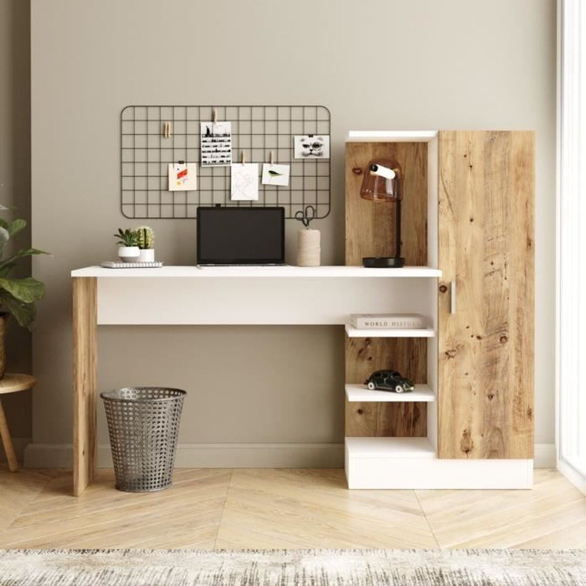 Ein moderner Schreibtisch mit Laptop, Lampe und Schrank. Es gibt ein Drahtgitter mit Bildern. Ein Mülleimer steht auf dem Boden.