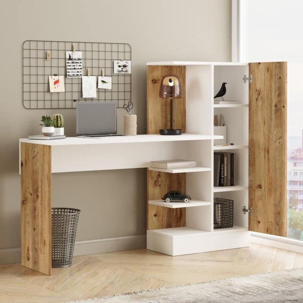 Ein moderner Schreibtisch mit Laptop, Lampe und Schrank. Über dem Schreibtisch hängt ein Drahtgitter mit Notizen, darunter ein Mülleimer.