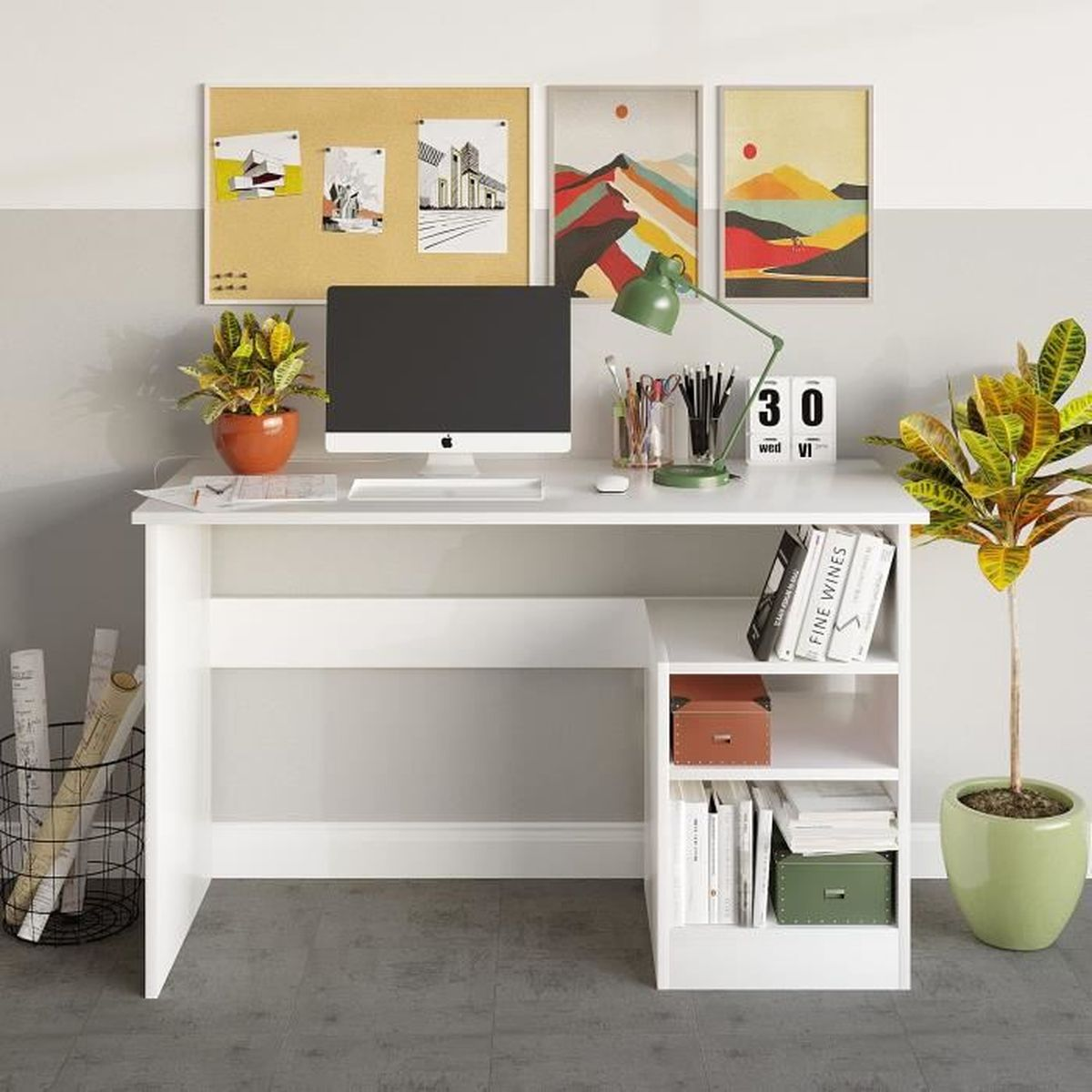 Ein weißer Schreibtisch mit Computer, Pflanzen und Büchern. Kunstwerke hängen darüber. Ein Drahtkorb und eine Topfpflanze stehen auf dem Boden.