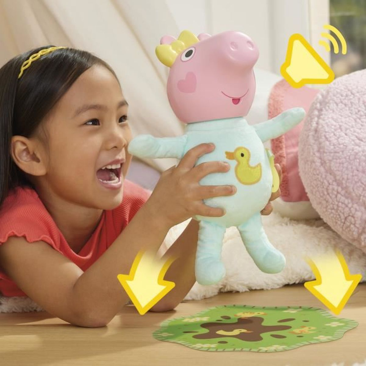 Ein Mädchen hält eine Peppa Wutz-Puppe und lächelt. Pfeile zeigen auf eine Schlammpfützen-Matte. Grafik mit Schallwellen neben der Puppe.