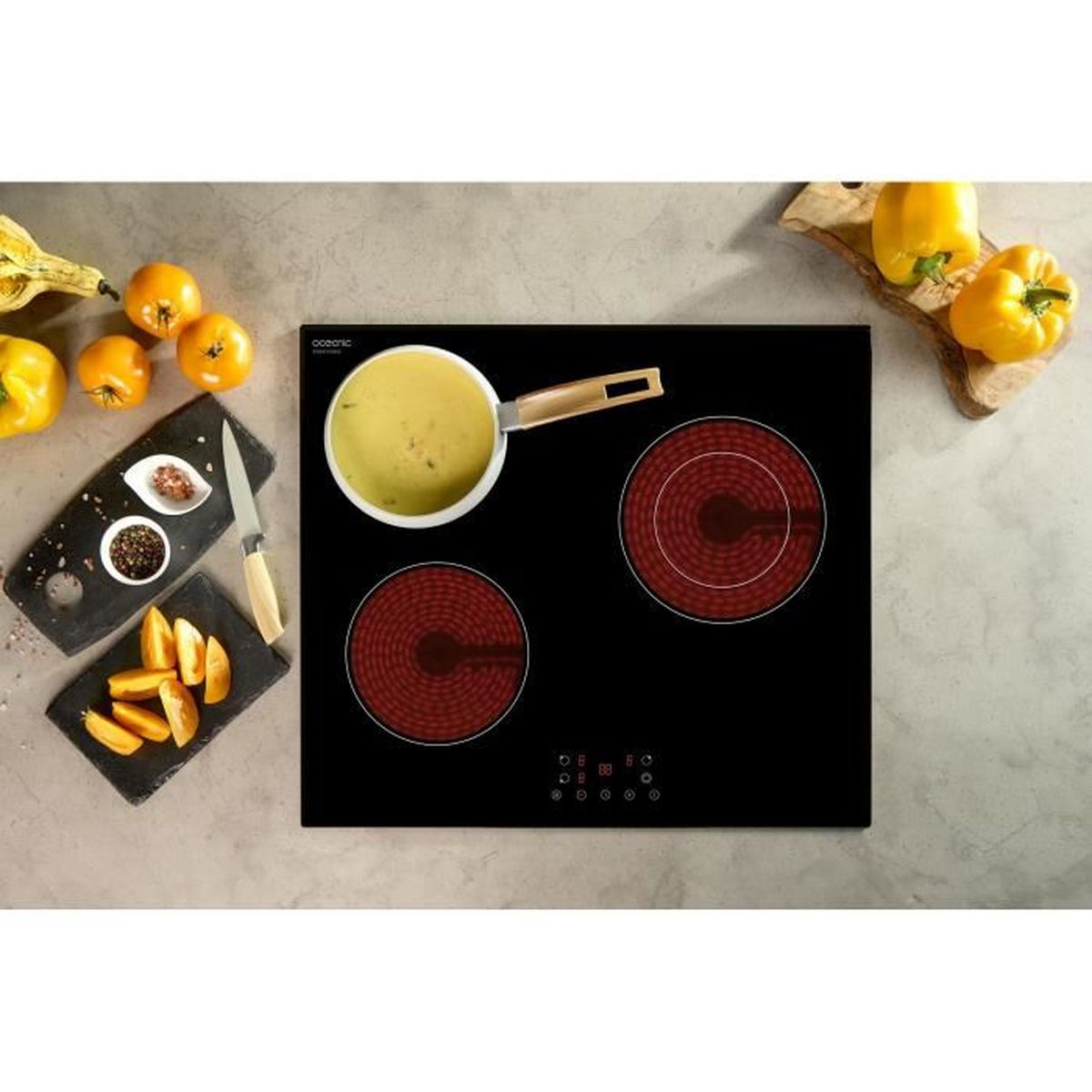 Un piano cottura nero con elementi riscaldanti rossi. Una pentola con zuppa è sul piano cottura. Sono presenti anche peperoni e pomodori gialli.