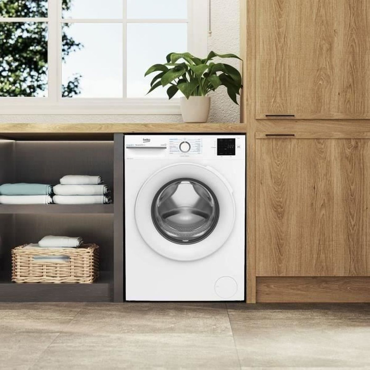 Eine weiße Waschmaschine steht in einem Holzschrank. Oben steht eine Pflanze. Links sind Regale mit gefalteten Handtüchern und einem Korb.