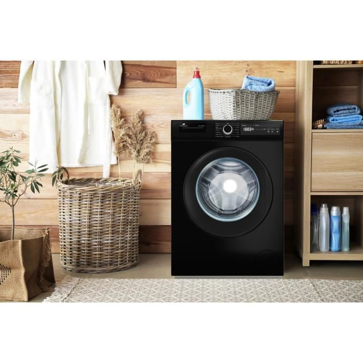 Eine schwarze Waschmaschine steht in einem Waschraum. Ein Bademantel hängt an der Wand. Körbe, Handtücher und Reinigungsmittel sind in der Nähe.