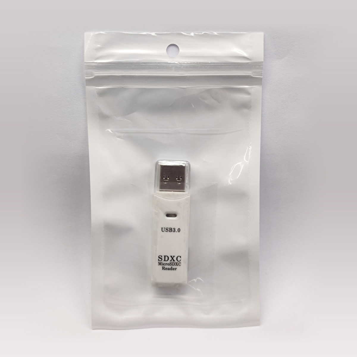 Ein weißer USB 3.0 SDXC MicroSDXC Kartenleser in einer transparenten Plastiktüte auf weißem Untergrund.