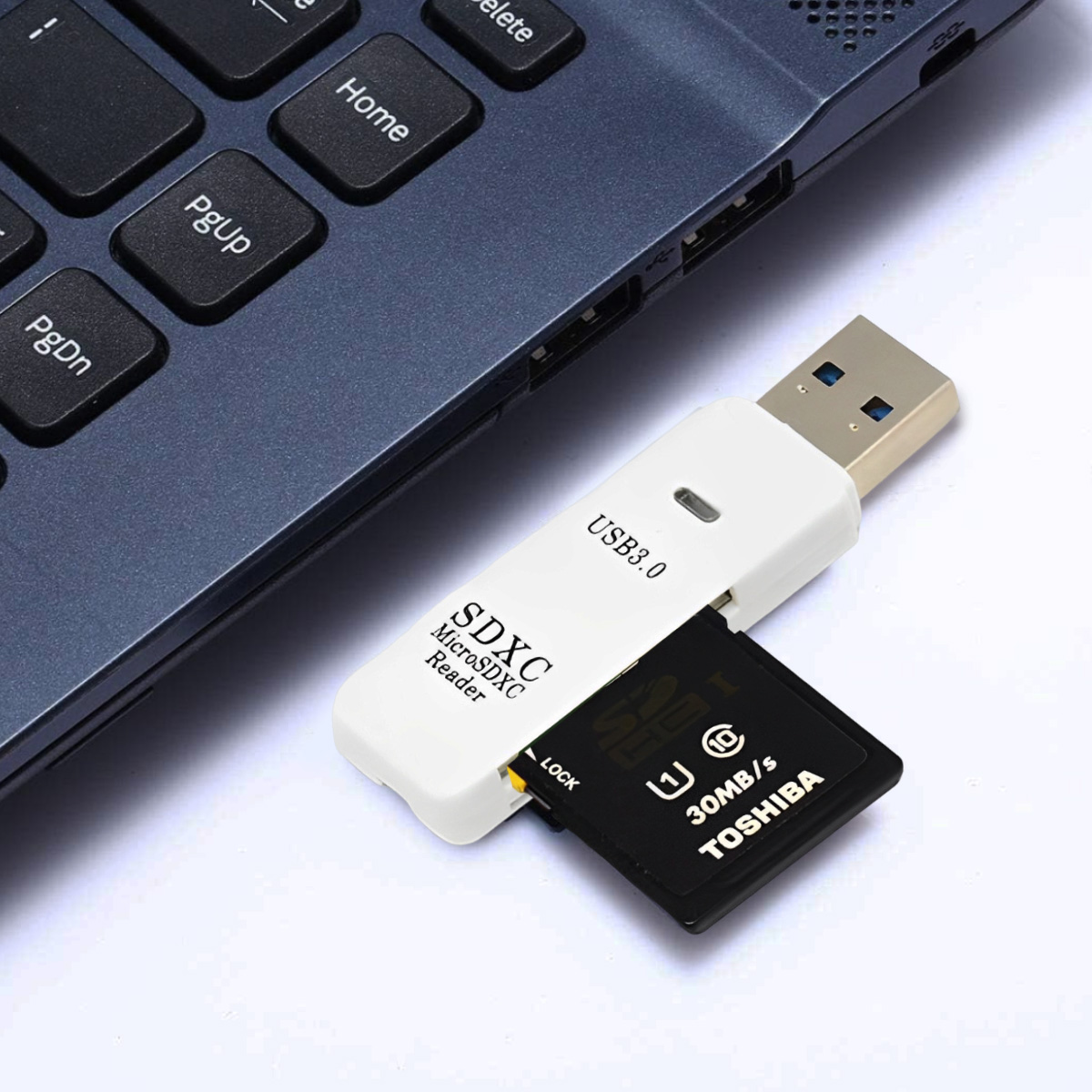 Ein weißer USB 3.0 SDXC-Kartenleser mit einer schwarzen SD-Karte, neben einer Laptop-Tastatur. Die Karte ist von Toshiba.
