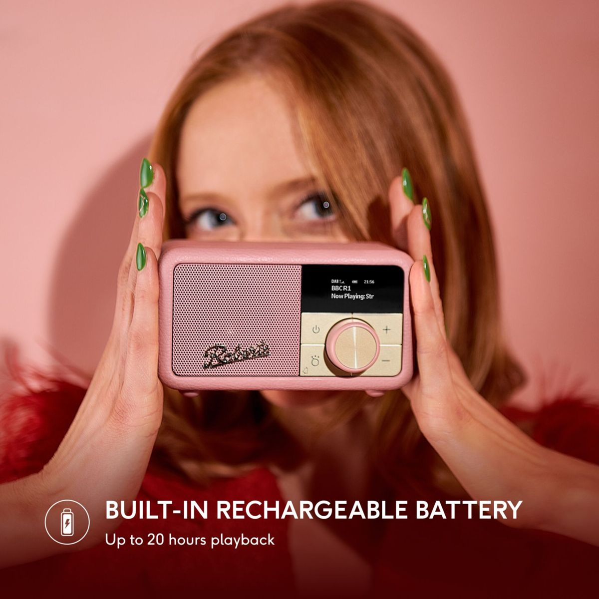 Eine Frau hält ein rosa Radio, ihre Augen sind sichtbar. Das Radio zeigt Informationen an. Grüne Nägel sind auffällig. Text: Eingebauter Akku.