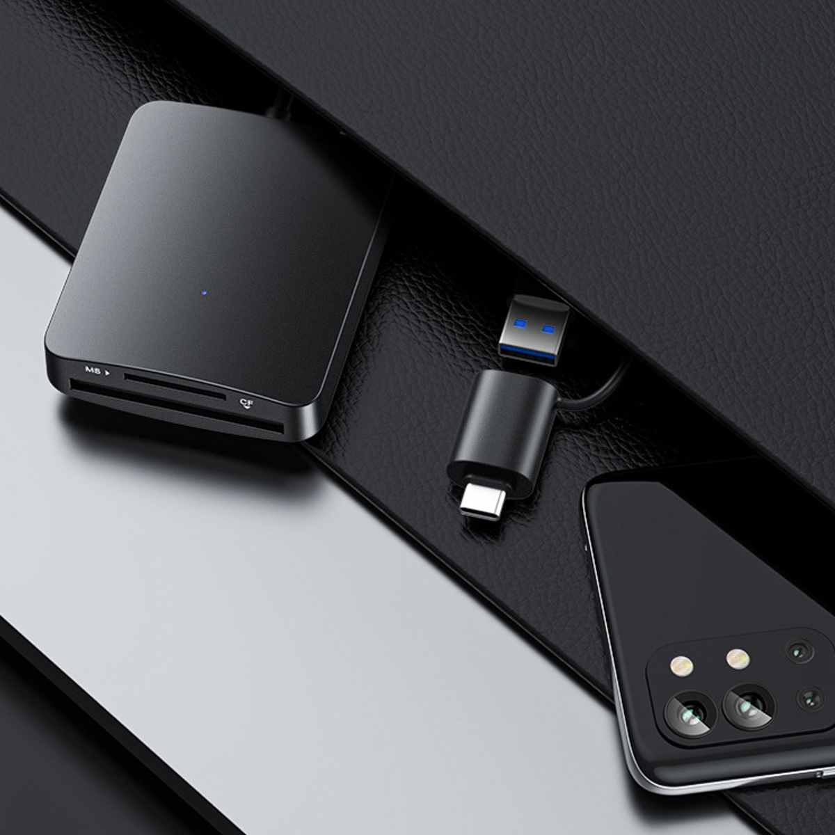 Schwarzes Kartenlesegerät, USB-C-Adapter und Telefon auf strukturierter Oberfläche. Das Telefon hat Kameras, und der Adapter hat einen USB-Anschluss.