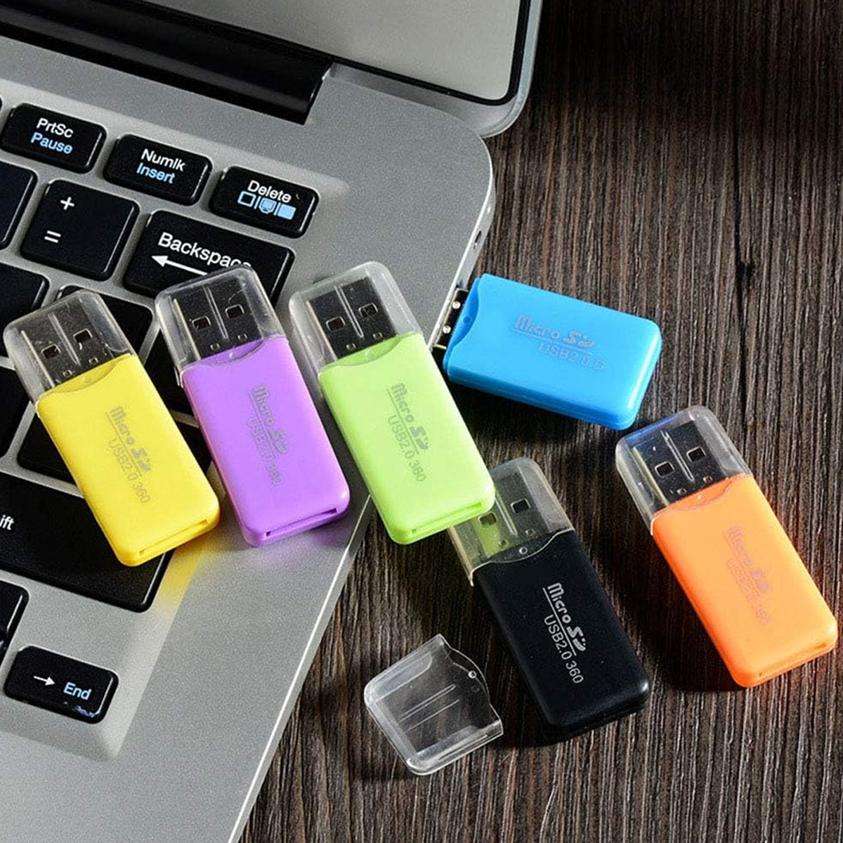 Bunte USB-Kartenleser liegen auf einer Laptop-Tastatur und einem Holztisch. Die Lesegeräte sind gelb, lila, grün, blau, schwarz und orange.