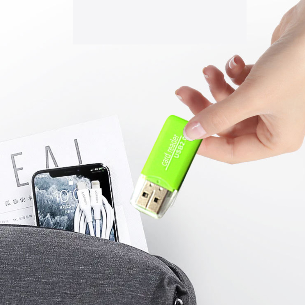 Eine Hand hält einen grünen Kartenleser. Ein Telefon und Kabel befinden sich in einer Tasche. Eine Magazinseite ist sichtbar.