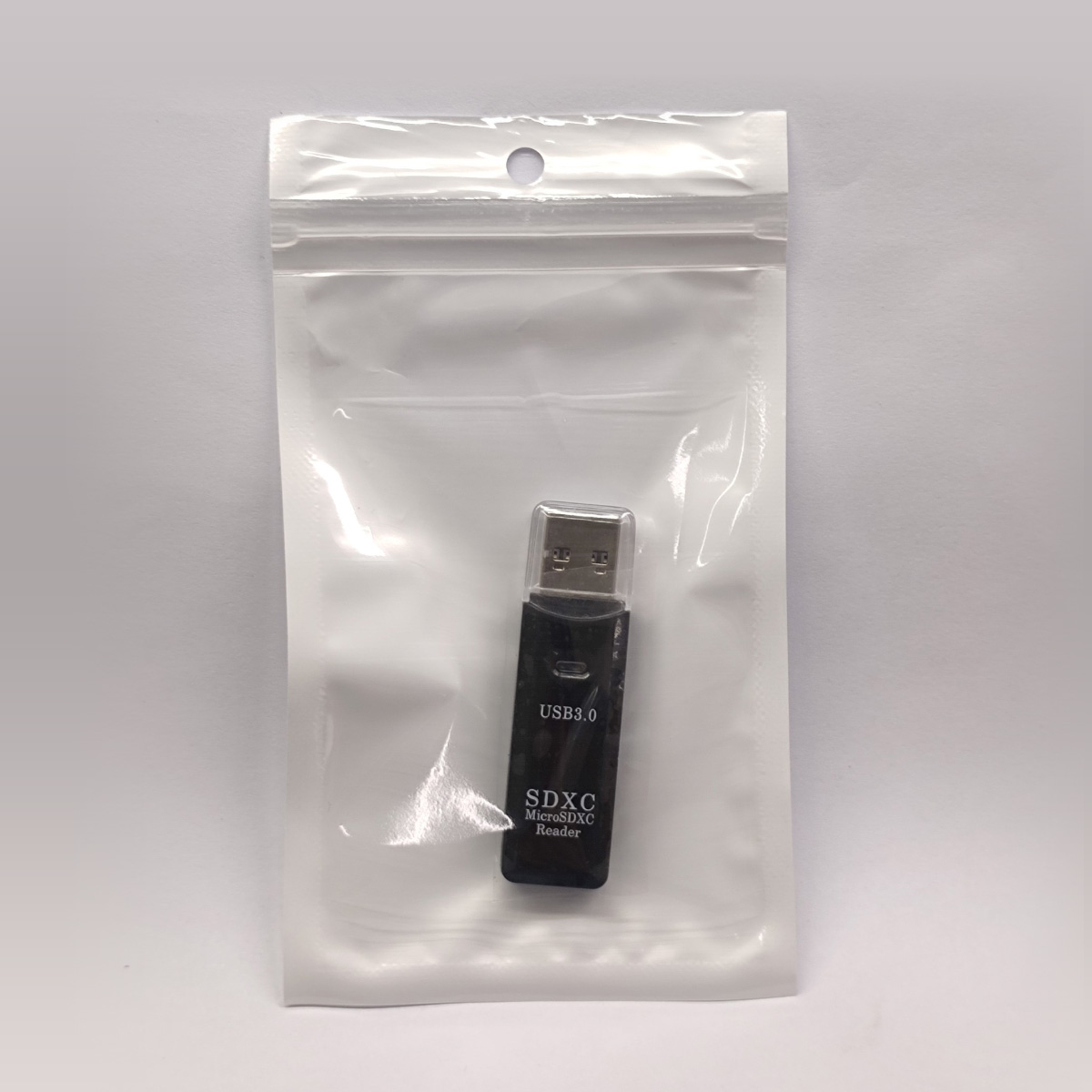 Ein schwarzer USB 3.0 SDXC MicroSDXC Kartenleser befindet sich in einer durchsichtigen Plastiktüte auf weißem Hintergrund.