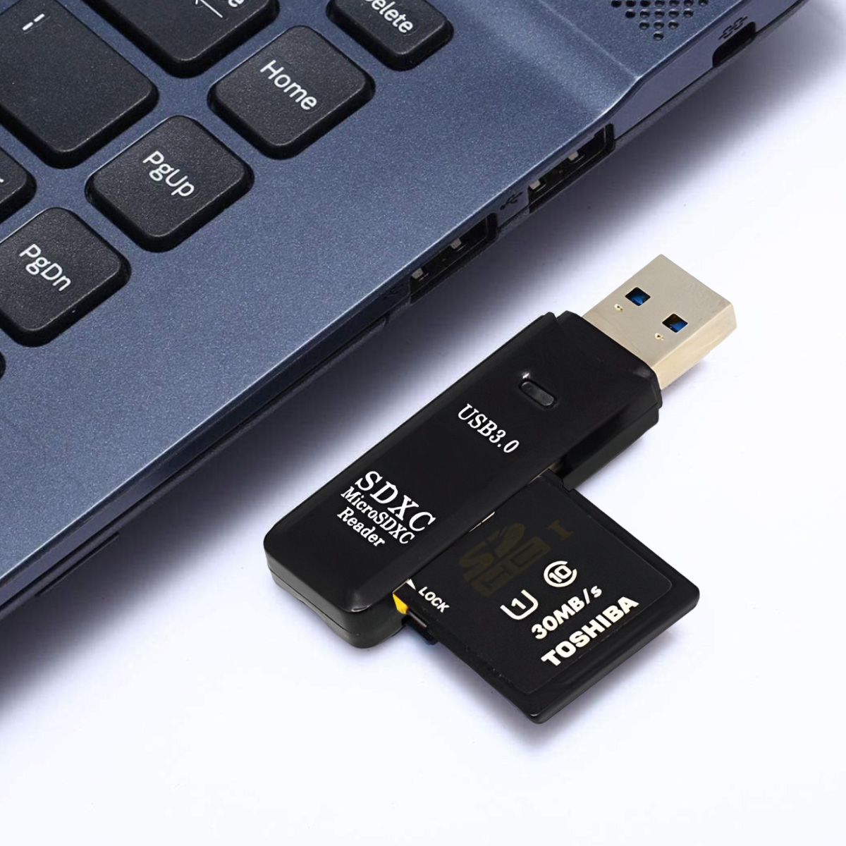 Ein schwarzer USB 3.0 SDXC-Kartenleser mit einer eingelegten Toshiba SD-Karte. Es liegt neben einer Laptop-Tastatur.