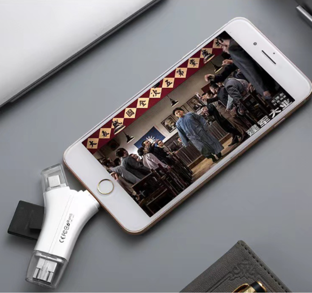 Ein Telefon zeigt eine Filmszene. Ein weißer Adapter ist angeschlossen. Ein Laptop und eine Brieftasche befinden sich im Hintergrund. Die Szene spielt in einem Gerichtssaal.