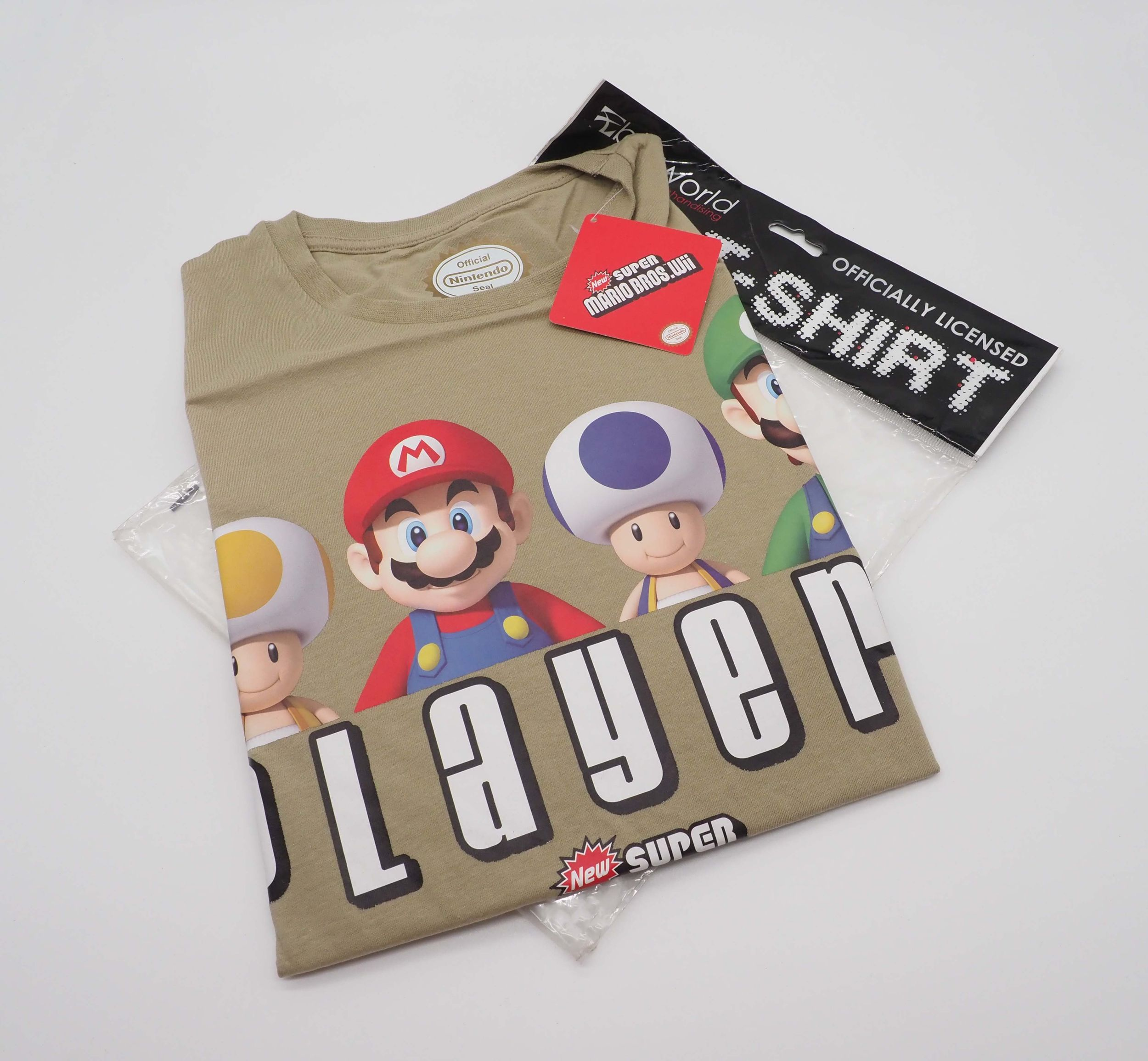 Ein hellbraunes T-Shirt mit Mario-Figuren, einem Etikett und einer Plastiktüte auf weißem Hintergrund.