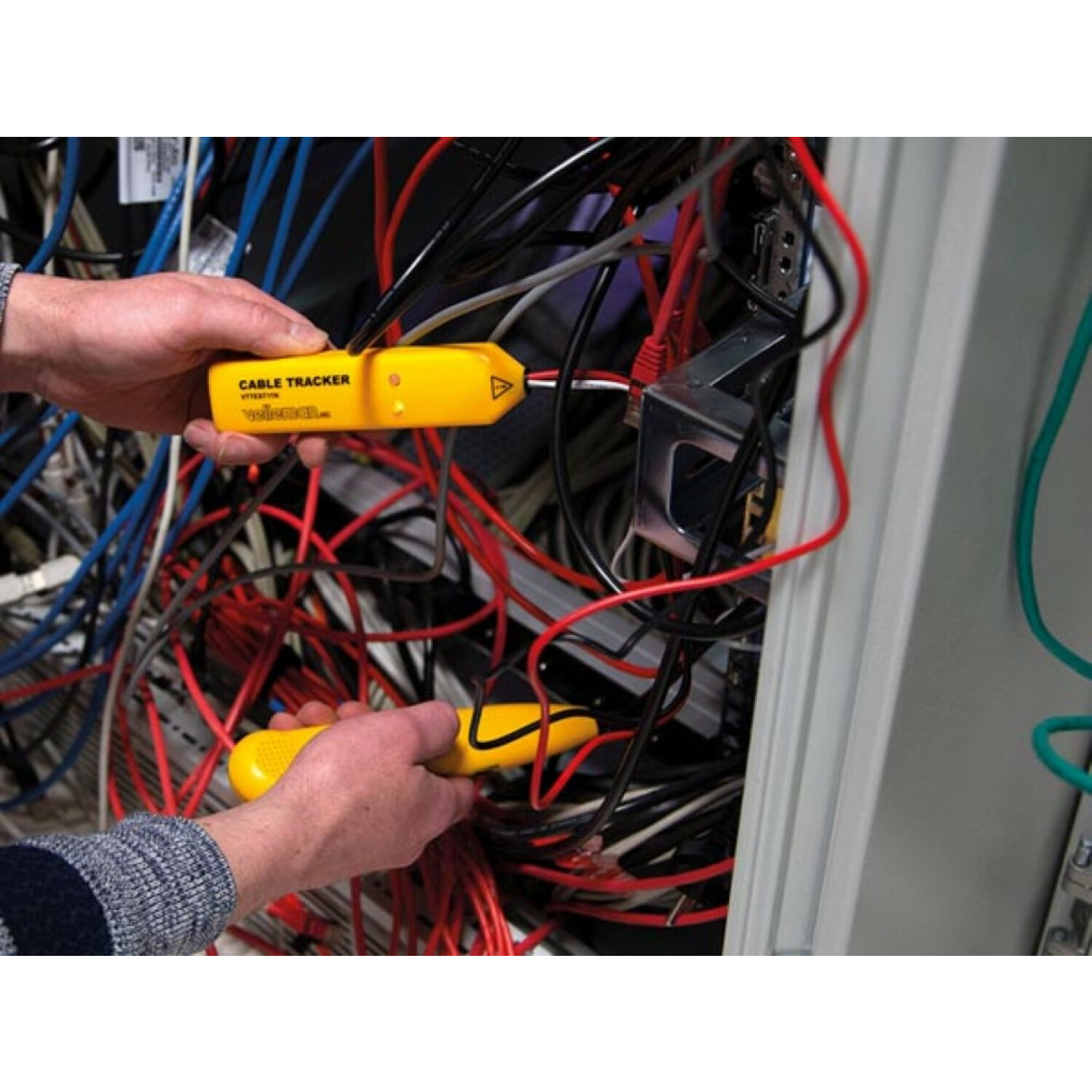 Hände, die gelbe Kabel-Tracker inmitten eines Netzwerkkabel-Chaos verwenden. Rote, blaue, schwarze und grüne Kabel sind im Serverraum zu sehen.
