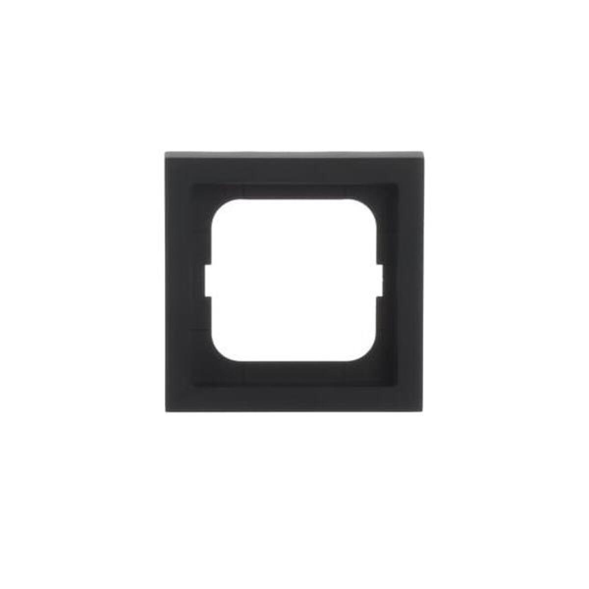 Un coperchio quadrato nero per presa elettrica con apertura quadrata al centro è centrato su sfondo bianco.