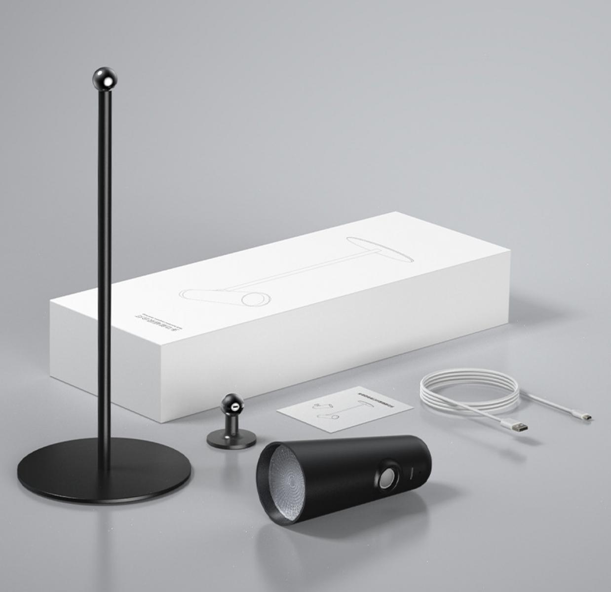 Eine schwarze Lampe, ein Ständer, eine Basis und ein kleiner Ständer befinden sich neben einer weißen Box und einem aufgerollten Kabel.